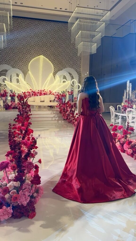 Engagement planner observes lavish stage with red floral aisle.